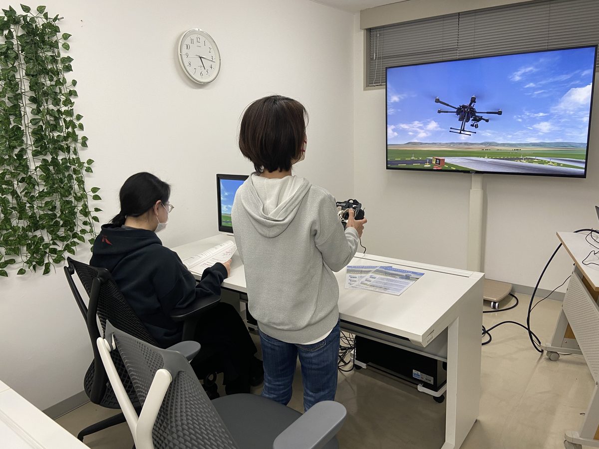 大きな画面を見ながら、シミュレーターで操縦を練習する受講者