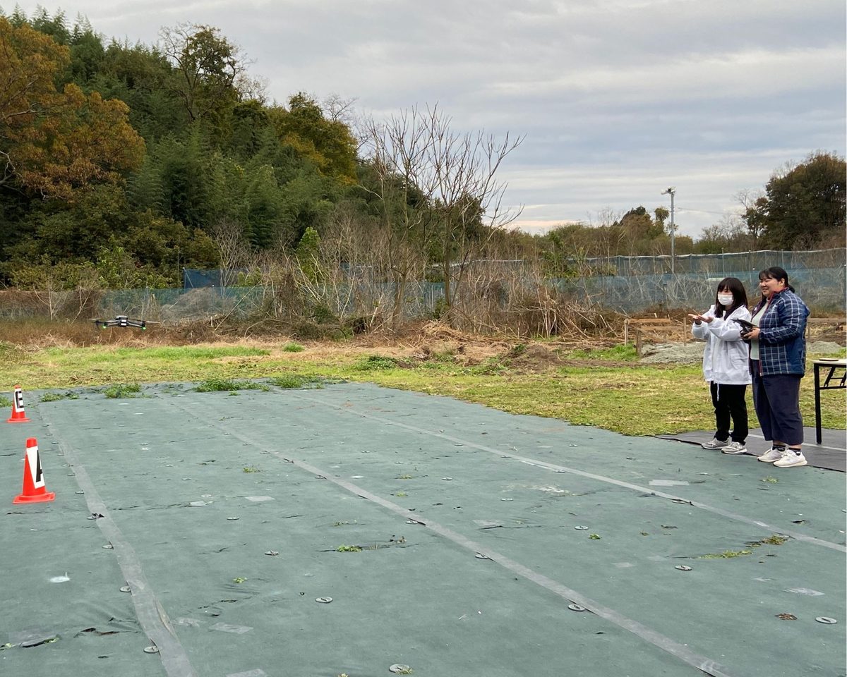 屋外会場の端に立ち、飛行している機体を見ながら操縦する2人