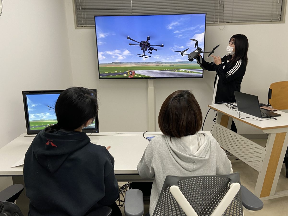 講師が機体を手に持ち、シミュレーターの画面を使って受講者に説明している様子