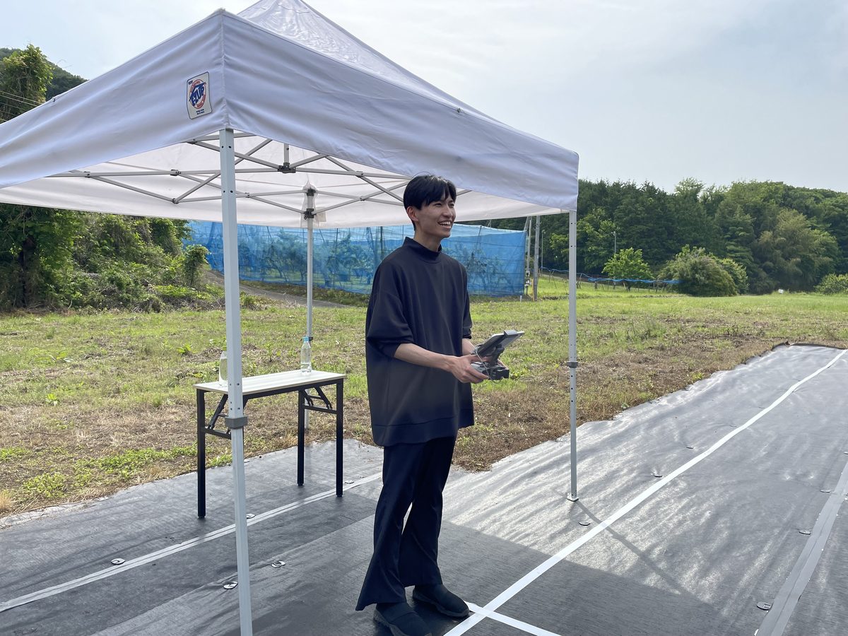 屋外会場のテントの下で、送信機を持って機体を操縦する受講者